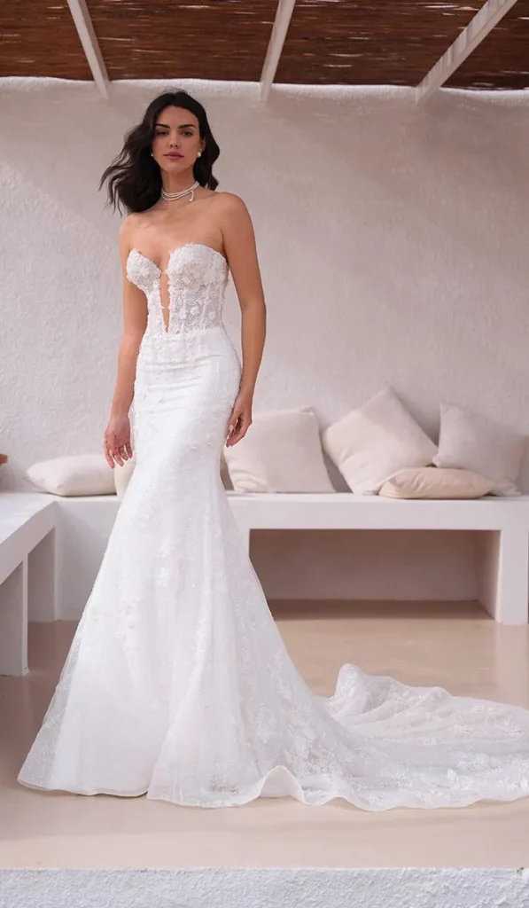Schulterfreies Brautkleid: Für Wen Passt Der Look Ohne Träger? 2 Braut In Einem Trägerlosen Mermaid-Hochzeitskleid Mit Tiefem Ausschnitt Und Spitzenverzierungen, Stehend Vor Einer Eleganten, Minimalistischen Kulisse.